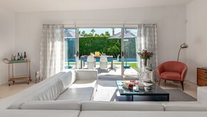 A modern living room with a large sofa, a coffee table, and a view of a pool and outdoor seating area. - PS Chill: Meticulous Mid-Century Features Modern Comfort and Views! (Palm Springs)