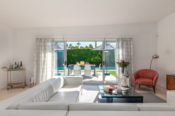 Una sala de estar moderna con un sofá grande, una mesa de centro y vistas a una piscina y una zona de estar al aire libre.