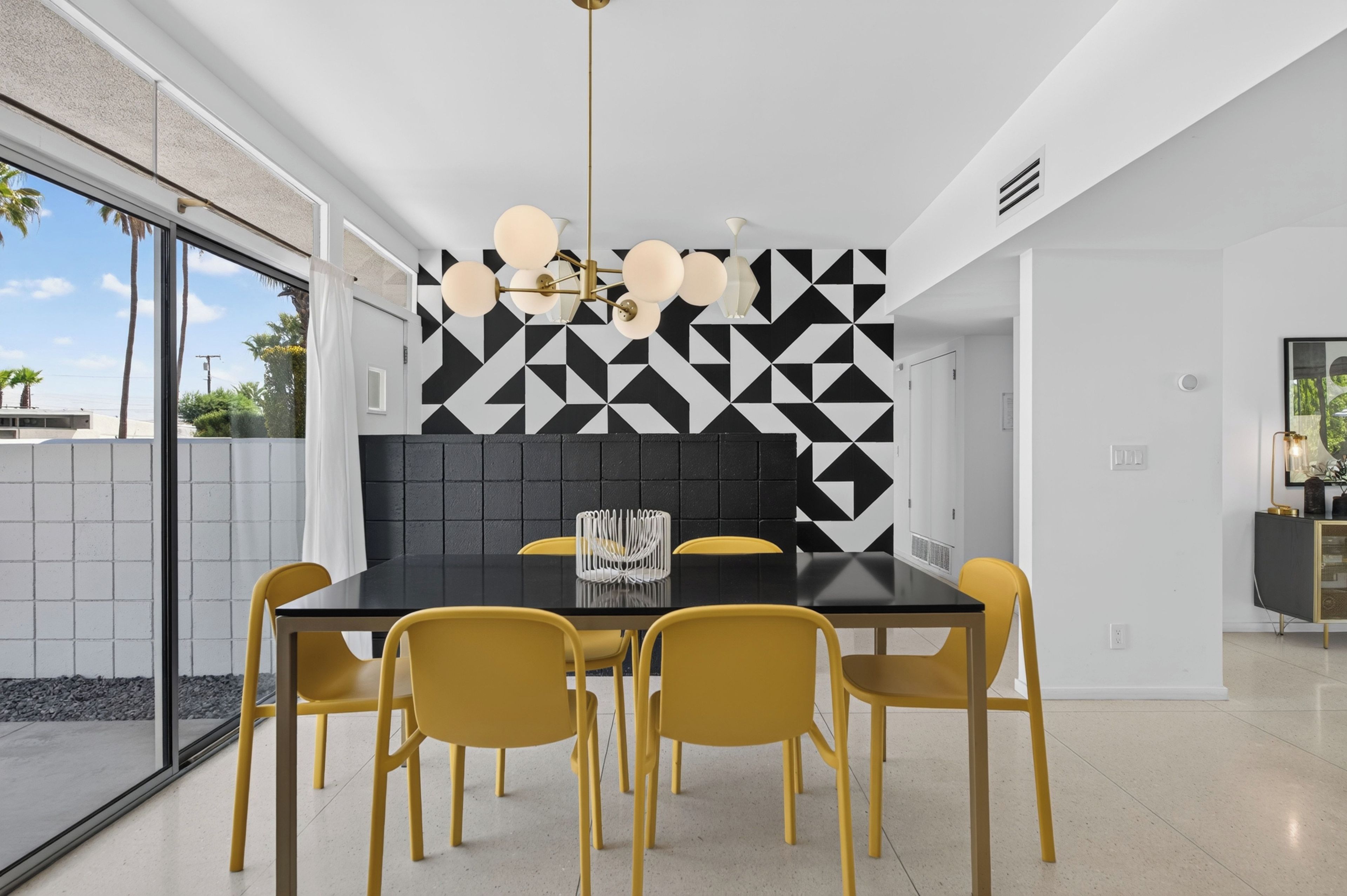 A modern dining area with a black table, yellow chairs, and a geometric patterned wall.