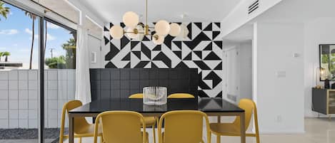 A modern dining area with a black table, yellow chairs, and a geometric patterned wall.