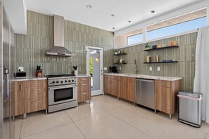A modern kitchen with stainless steel appliances, wooden cabinets, and a large window providing natural light.