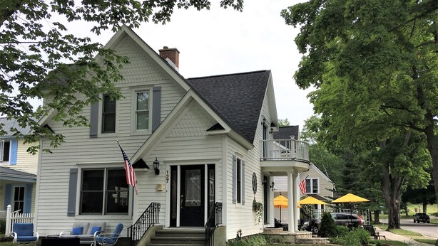 A two-story house with a front porch, a flag, and a small garden. - Steps To The Beach & 2 Blocks To Downtown Frankfort - Sleeps 6-8 (Frankfort)