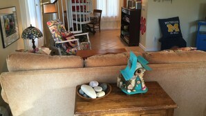A living room with a sofa, a wooden coffee table with a decorative birdhouse, a lamp, and a bookshelf. - Steps To The Beach & 2 Blocks To Downtown Frankfort - Sleeps 6-8 (Frankfort)