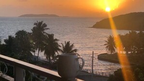 Un coucher de soleil sur une étendue d’eau, avec des palmiers et une terre lointaine à l’horizon.