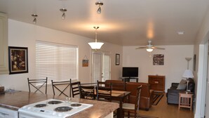 A modern kitchen with a stove, dining table, and chairs. There is a ceiling fan and a TV in the living area. - BEACHFRONT PRIVATE COTTAGE, FULL FLOOR, DECK, FREE PARKING BY ENTRANCE, 2BD 2BA  (Panama City Beach)