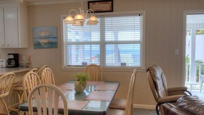 A dining area with a table set for four, surrounded by wooden chairs. There is a window with blinds, a painting on the wall, and a ceiling light fixture. - BEACHFRONT PRIVATE COTTAGE, FULL FLOOR, DECK, FREE PARKING BY ENTRANCE, 2BD 2BA  (Panama City Beach)