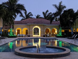 A hotel with a swimming pool, palm trees, and a tiled roof.