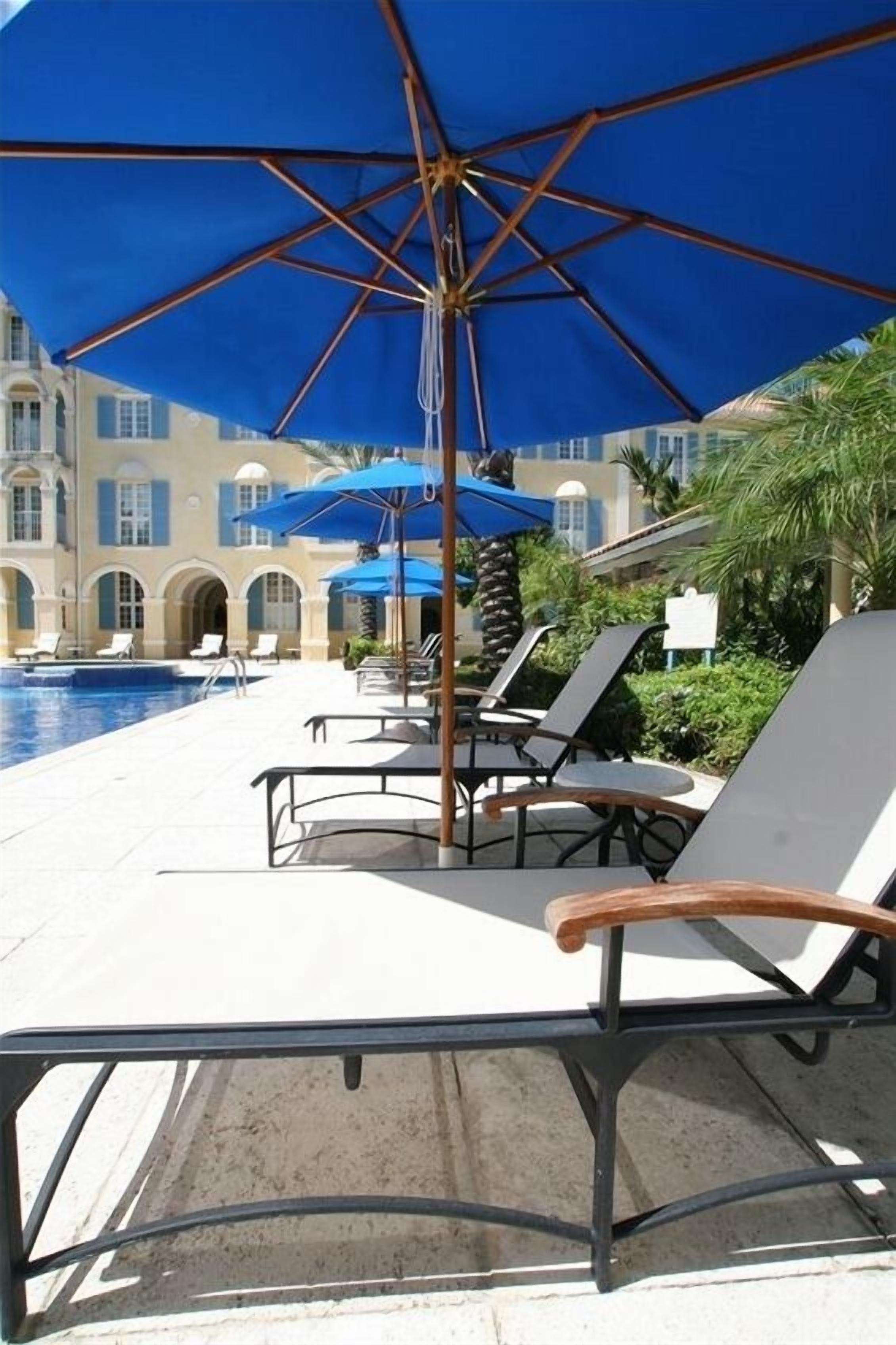 Un espace aménagé au bord de la piscine, avec des chaises longues et des parasols, une piscine, et un bâtiment aux fenêtres en arc de cercle en arrière-plan.
