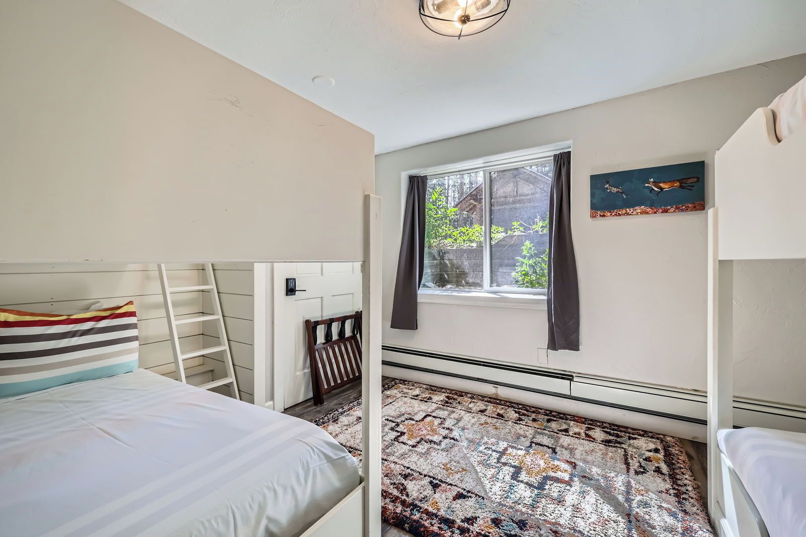 A bedroom with bunk beds, a window with curtains, a patterned rug, and a door with a keypad lock.