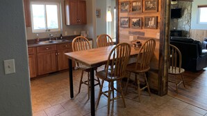 A kitchen with wooden cabinets, a dining table with chairs, and a stone wall with framed pictures.