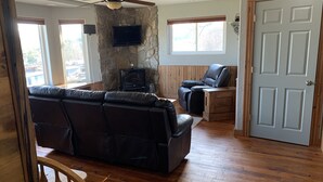 A living room with a stone wall, a fireplace, a leather sofa, a recliner, and a television.