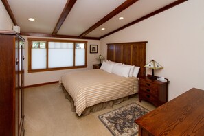 A bedroom with a bed, wooden headboard, bedside table, lamp, and a window with blinds.