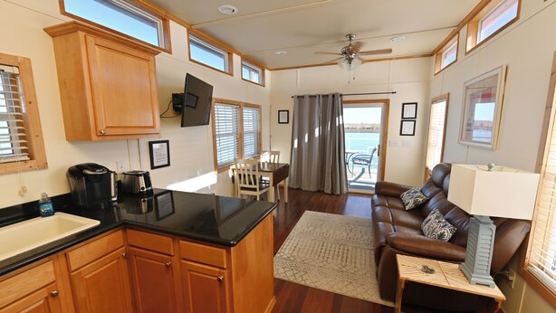 A spacious kitchen with wooden cabinets, a black countertop, and a ceiling fan. There is a dining area with a brown leather couch and a small table. - Rebel's Rest - A Romantic Getaway Houseboat w/ New Water Filtration System (Apalachicola)