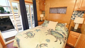 A bedroom with a bed, a nightstand, a window with curtains, and a view of the outside. - Rebel's Rest - A Romantic Getaway Houseboat w/ New Water Filtration System (Apalachicola)