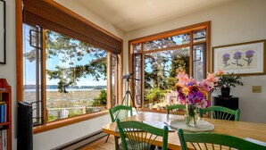 Comedor con una mesa de madera, sillas verdes y vista a un cuerpo de agua a través de amplias ventanas.