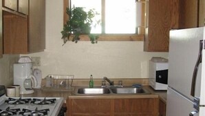 Une cuisine de taille réduite, dotée de meubles en bois, d’une cuisinière à gaz, d’un évier et d’un réfrigérateur.