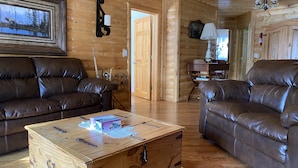 A log cabin interior with two leather sofas, a wooden coffee table, and a mounted picture. - Beautifully secluded getaway perfect for all seasons! (Adams)
