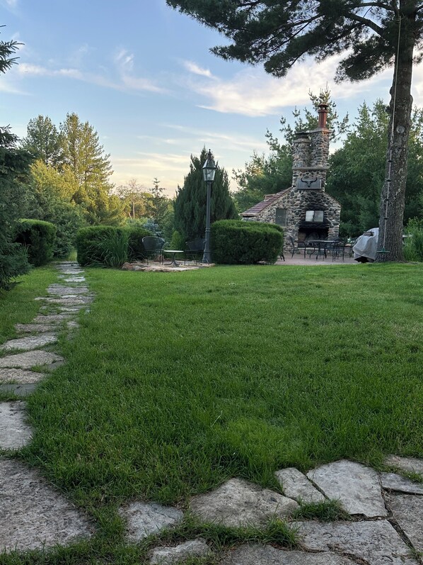 A stone pathway leading to a stone building with a chimney, surrounded by well-maintained grass and trees. - Beautifully secluded getaway perfect for all seasons! (Adams)