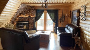 A cozy log cabin interior with a stone fireplace, leather sofas, and a wooden ceiling. - Beautifully secluded getaway perfect for all seasons! (Adams)