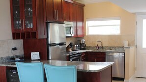 A modern kitchen with wooden cabinets, stainless steel appliances, and a central island with chairs. - 3 Bedroom Cayman Condo on Seven Mile Beach!  (George Town)