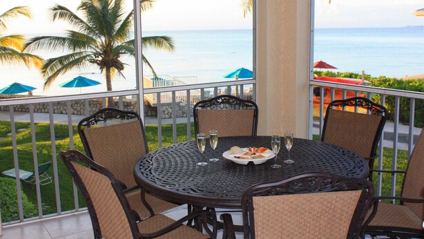 A round table with four chairs, two wine glasses, and a plate with food. - 3 Bedroom Cayman Condo on Seven Mile Beach!  (George Town)