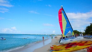 A beach with a sailboat, kayaks, and people swimming. - 3 Bedroom Cayman Condo on Seven Mile Beach!  (George Town)