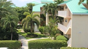 A hotel with a green roof, a balcony, and a well-maintained garden with palm trees and hedges. - 3 Bedroom Cayman Condo on Seven Mile Beach!  (George Town)