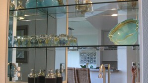 Una cocina con un armario de vidrio que exhibe diferentes vasos y un lavamanos de acero inoxidable.