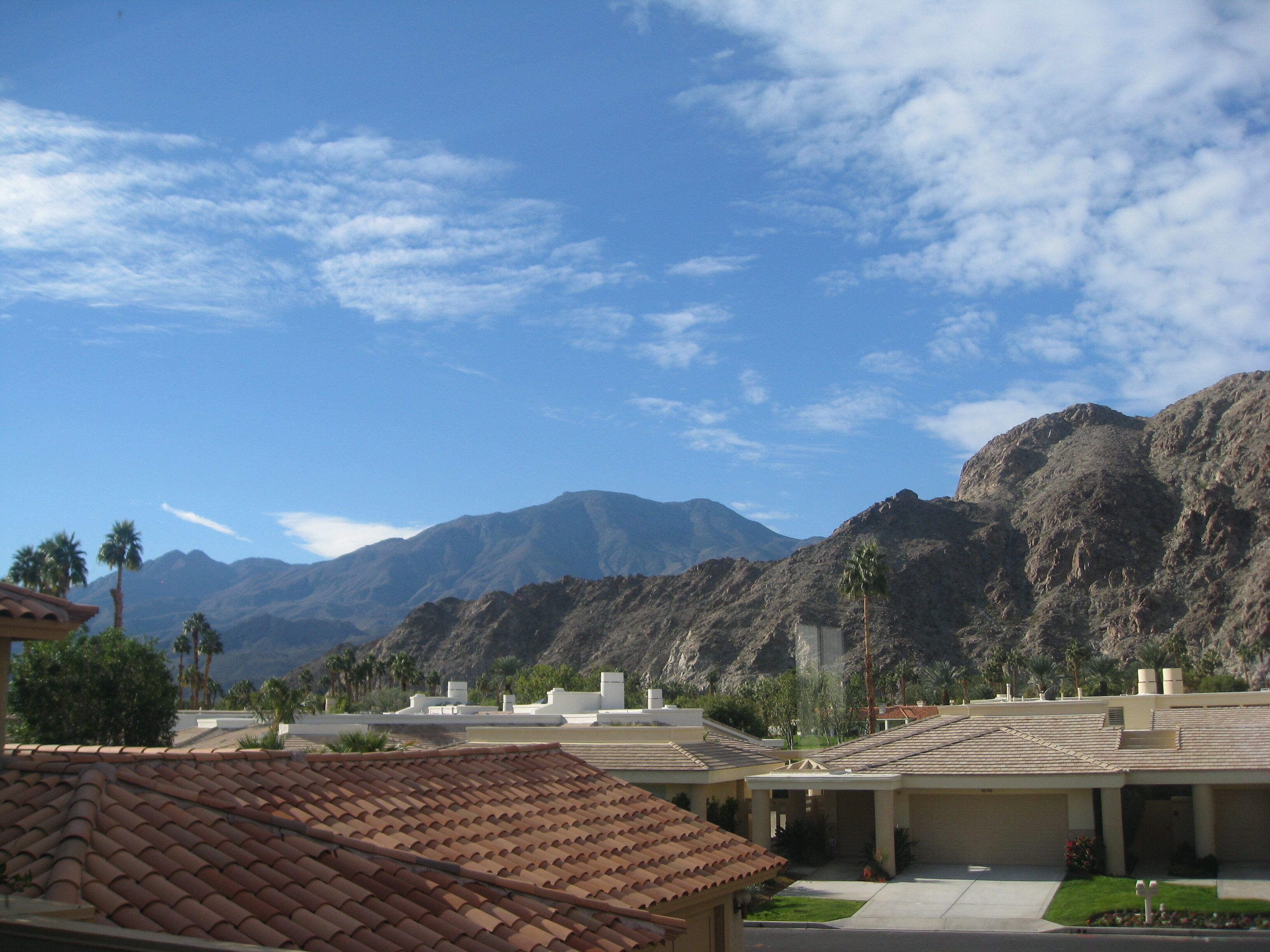 Un barrio residencial con casas de tejas de terracota, cielo azul despejado y montañas al fondo.