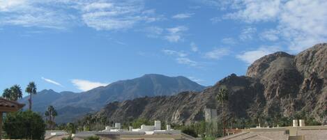 A residential area with houses featuring terracotta roofs, a clear blue sky, and mountains in the background.