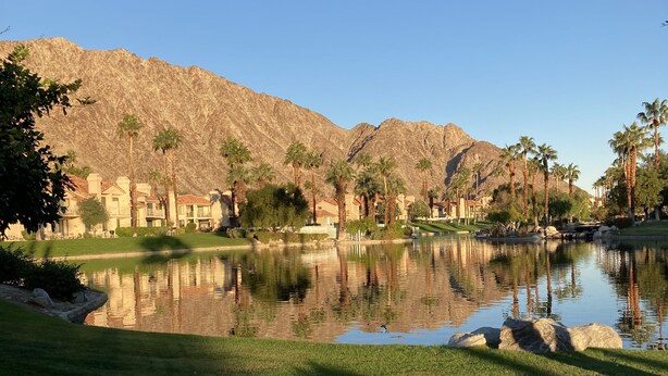Un paisaje sereno con un lago, palmeras y montañas al fondo.