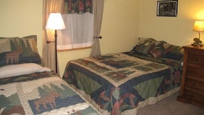 A bedroom with two beds, a nightstand, a lamp, a dresser, and a window with curtains.