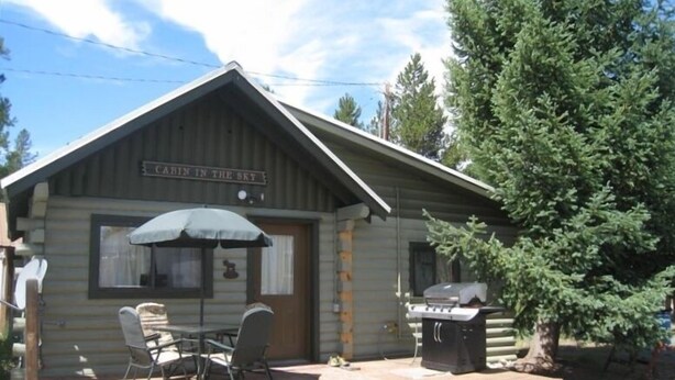 A cabin with a porch, a table and chairs, a grill, and a sign that reads "Cabin in the Sky".