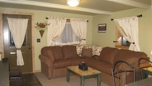 A living room with a brown sofa, a wooden coffee table, and a dining area with a metal chair and a table.