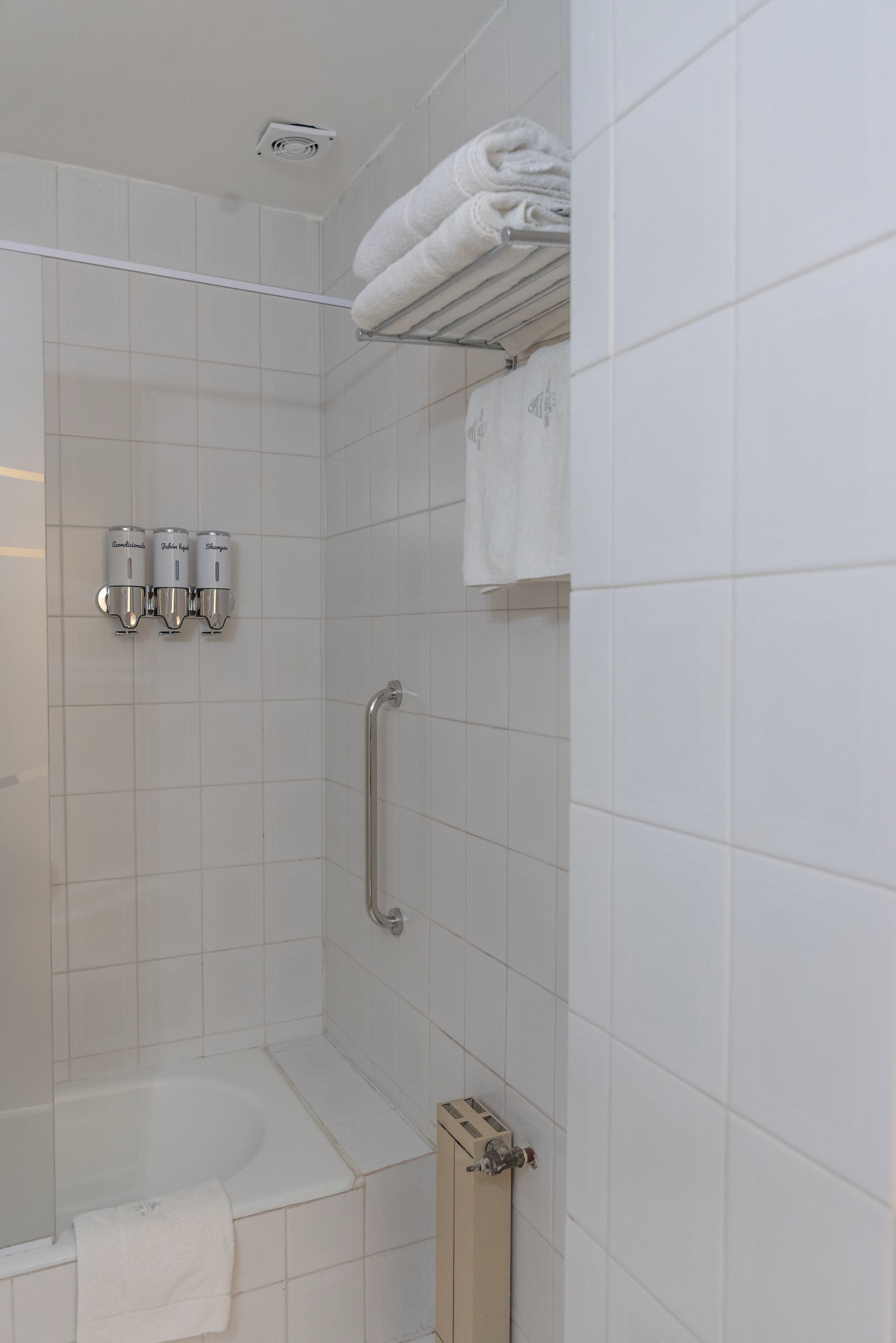 Un baño moderno con cabina de ducha, barra de apoyo y tres dispensadores de jabón para manos.