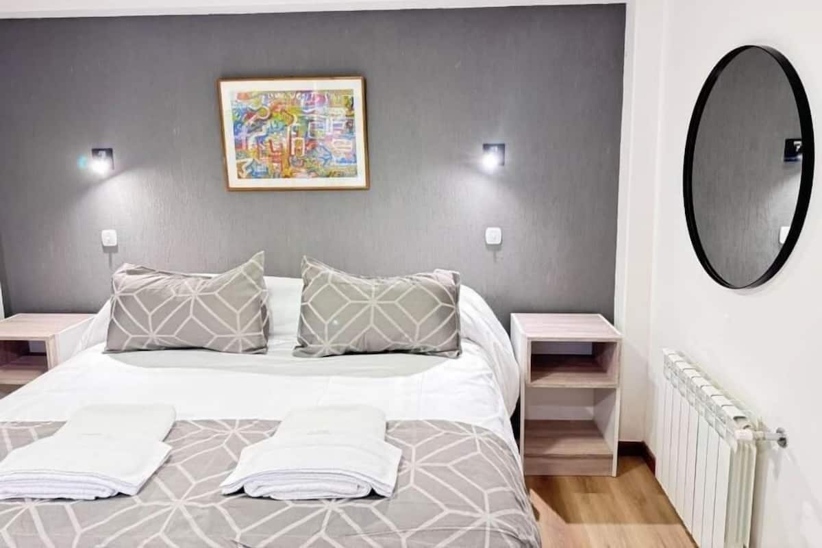Een slaapkamer met een bed, twee nachtkastjes, een spiegel en een aan de muur bevestigd schilderij.
