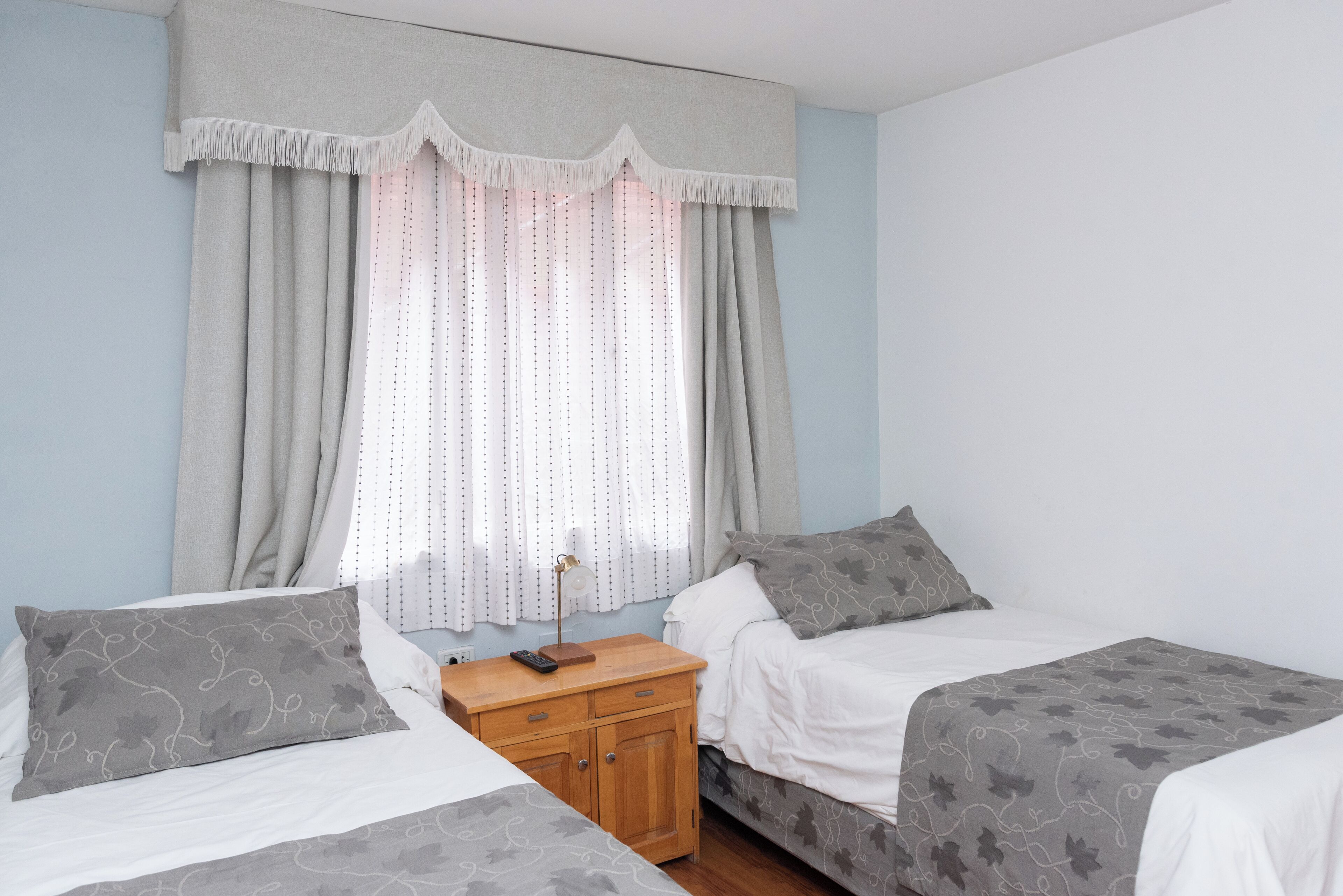 Une chambre avec deux lits, une table de chevet et une fenêtre avec des rideaux.