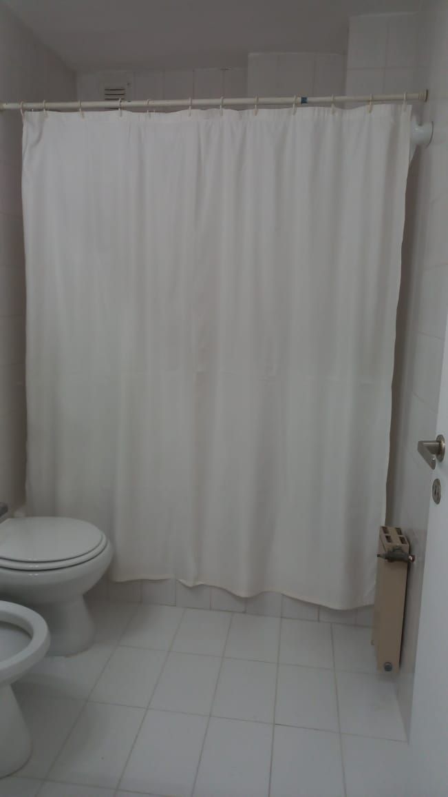 Une salle de bain avec des toilettes blanches, un rideau de douche et un sol carrelé.