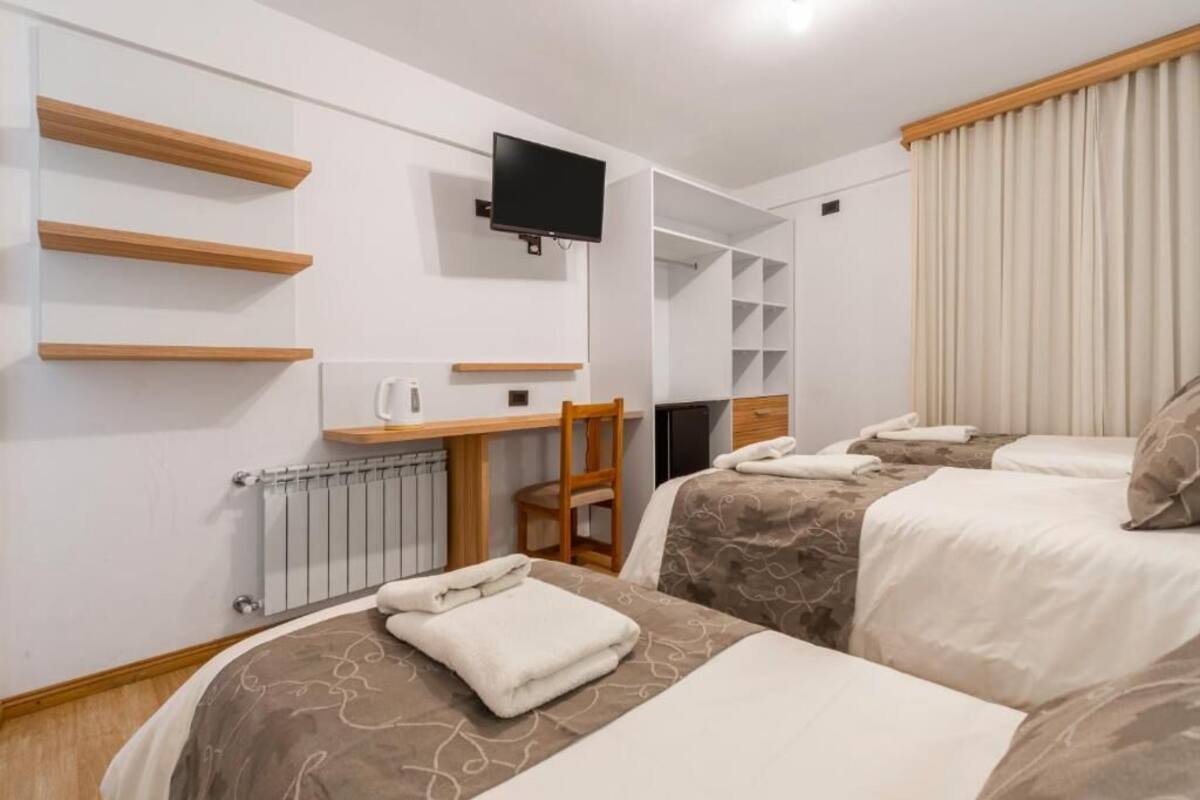 Een hotelkamer met twee bedden, een bureau, een stoel, een televisie en inbouwplanken.