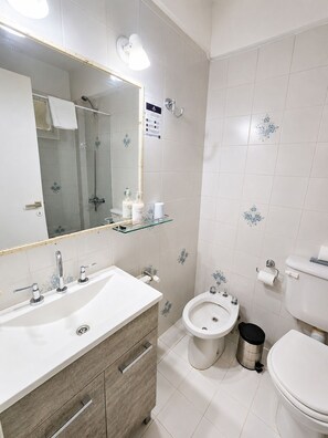 A modern bathroom with a large mirror, a glass shelf, a sink, a bidet, and a toilet.
