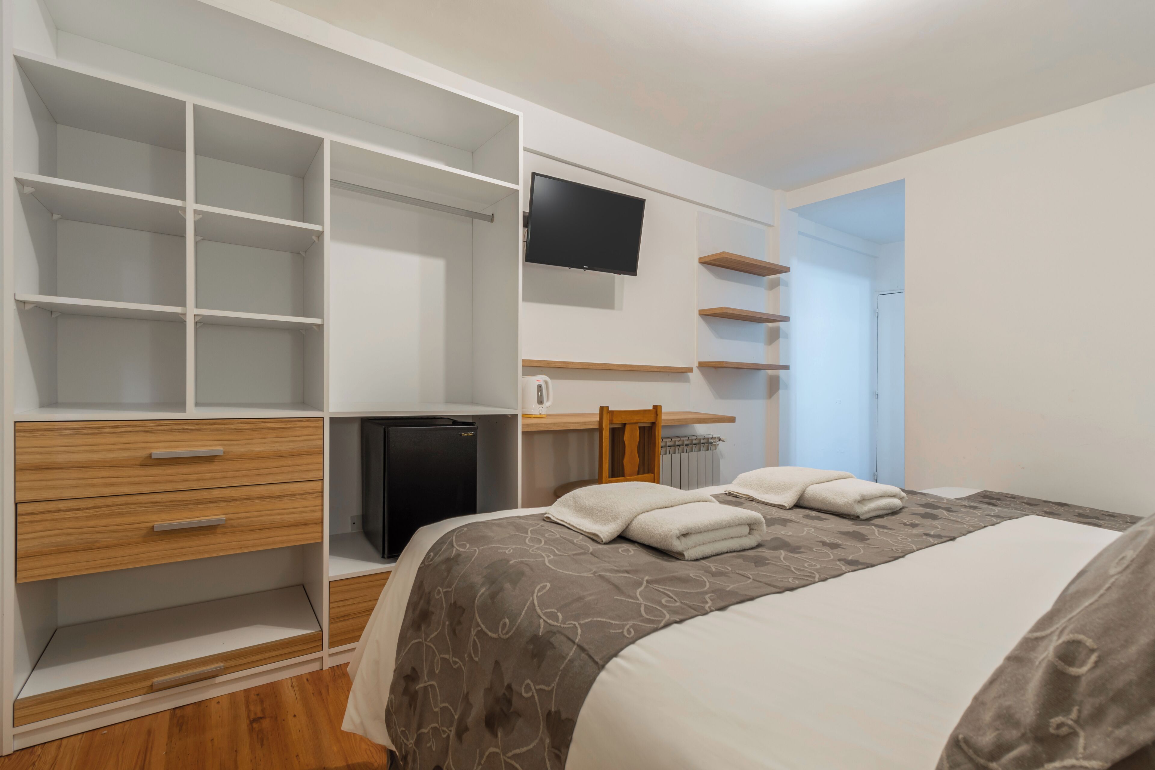 Un dormitorio con cama, escritorio, televisión y almacenamiento integrado.
