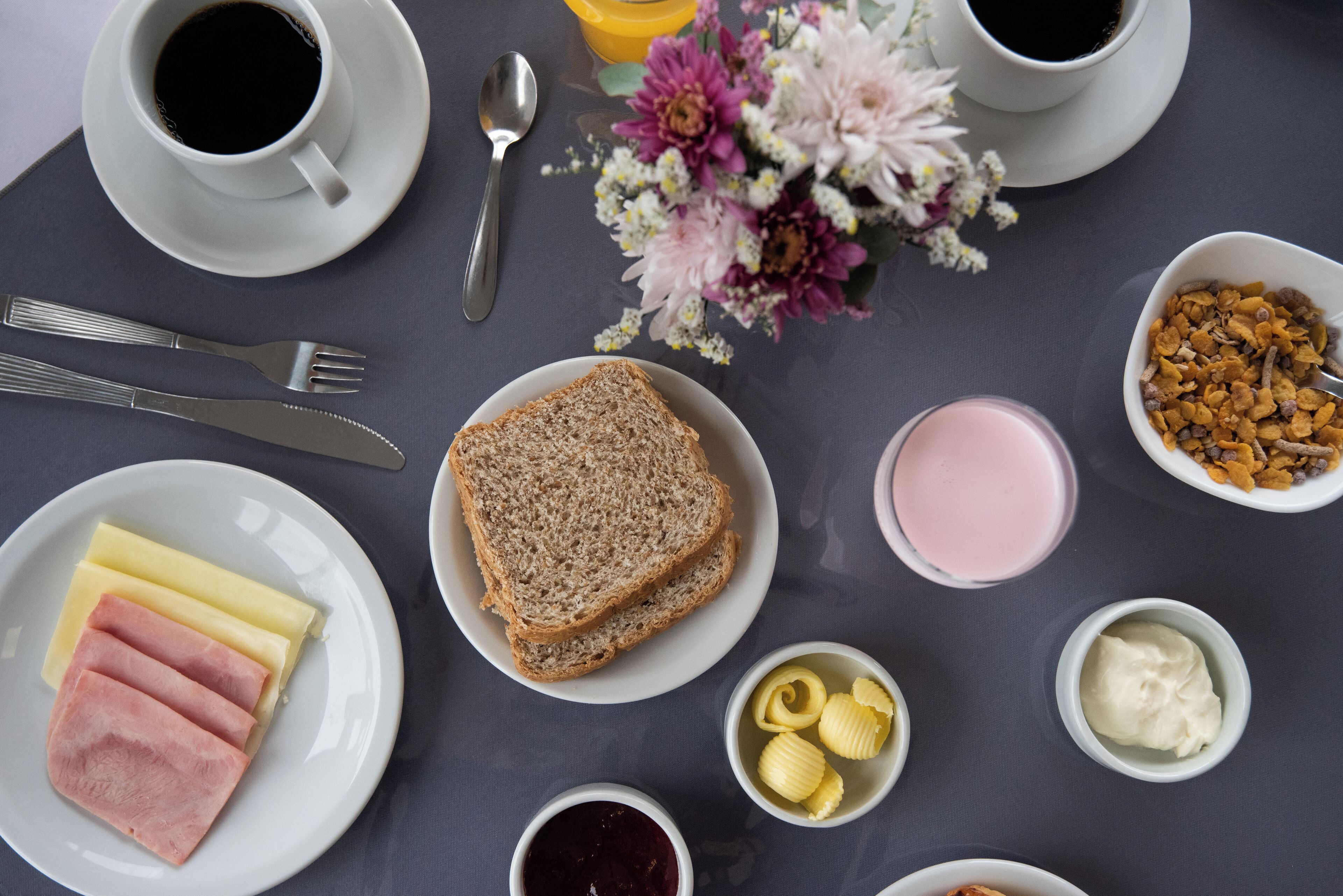 En frukostuppdukning med bröd, skinka, smör, sylt och en blomsterdekoration.
