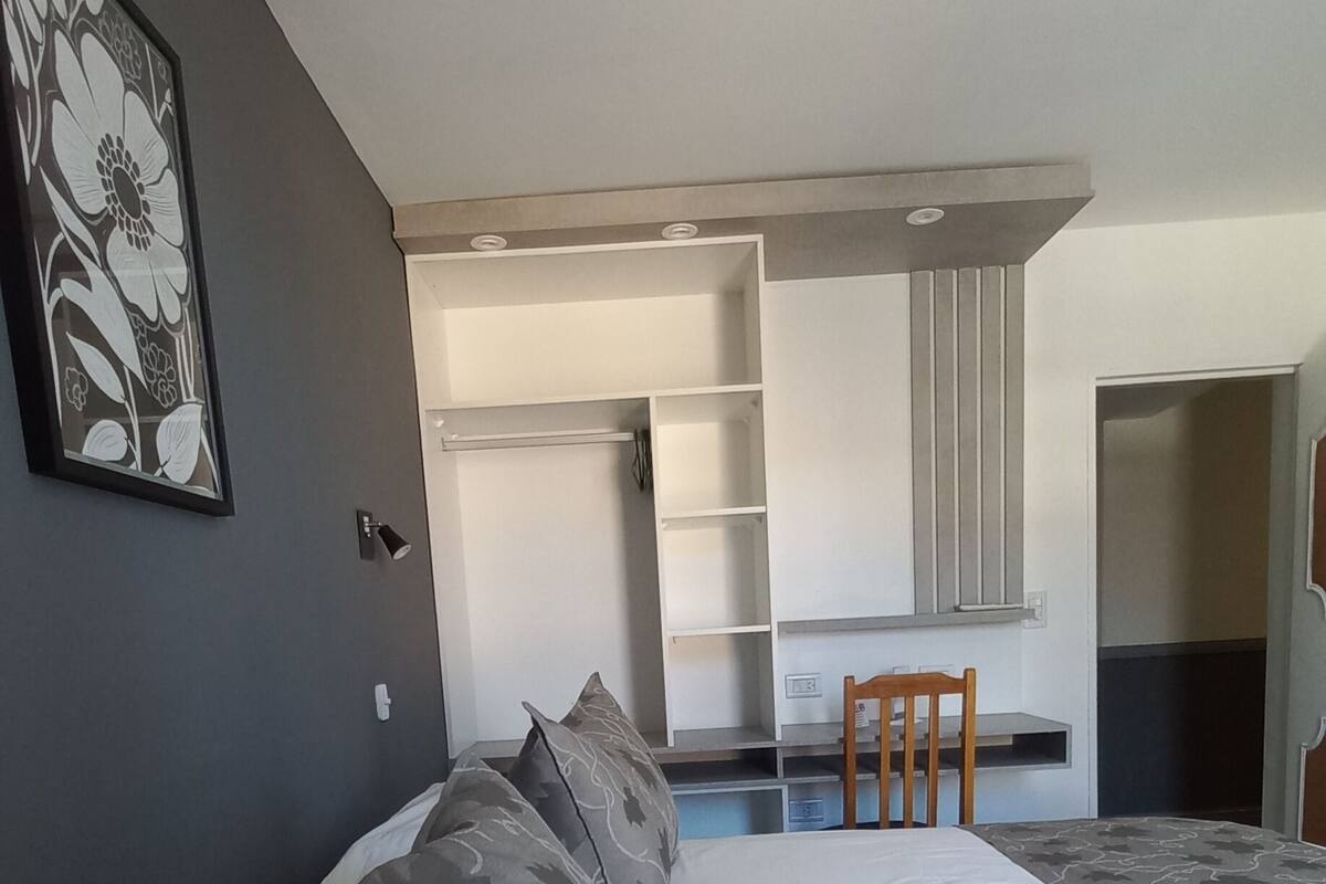 Een moderne slaapkamer met een groot bed, een bureau en een stoel. Er is een kledingkast en een deur naar een andere kamer.
