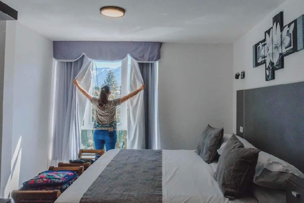Een slaapkamer met een bed, een raam met gordijnen, een nachtkastje en een aan de muur hangend kunstwerk.