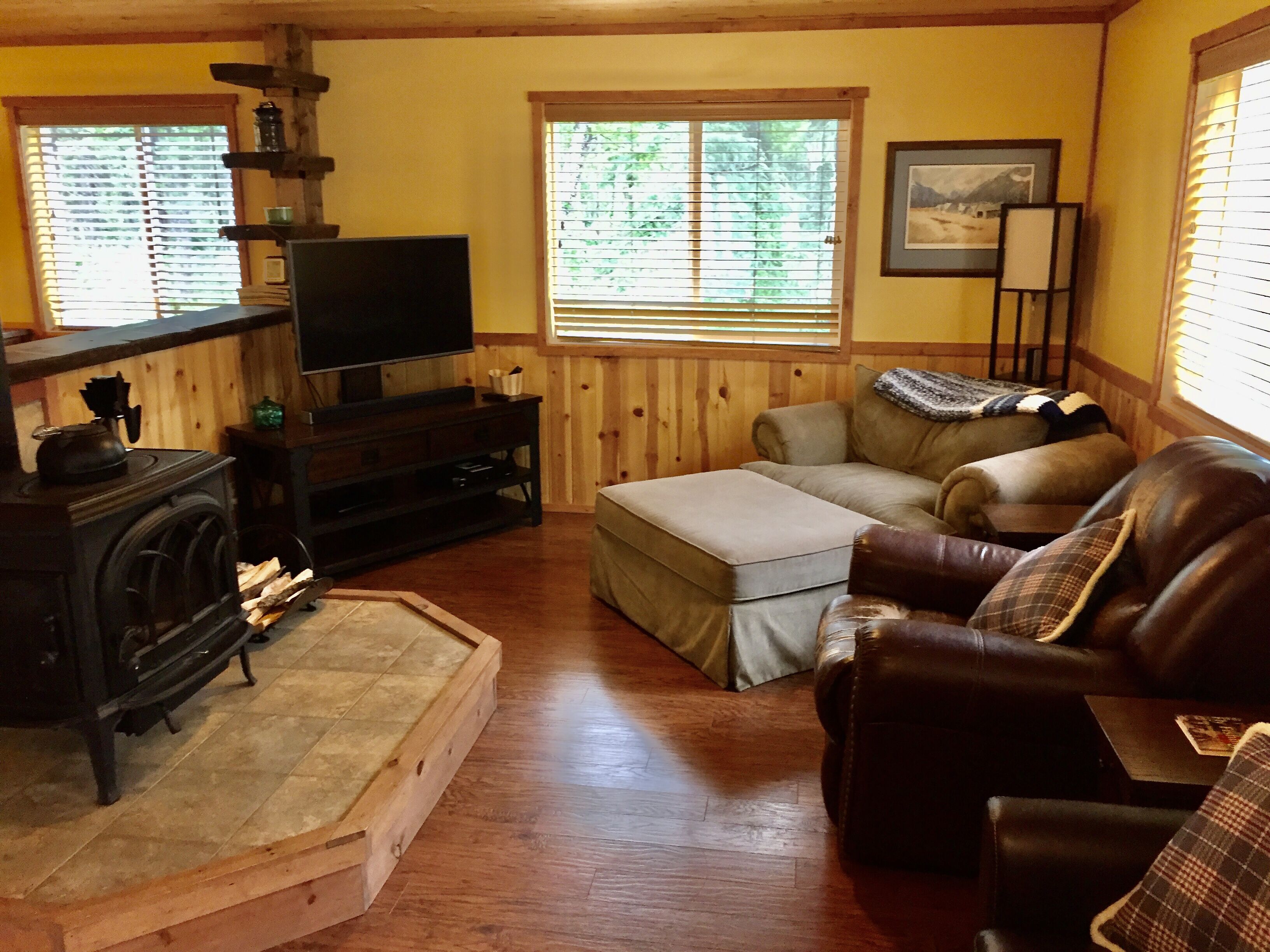 A cozy living room with a fireplace, a sofa, a television, and a window with blinds.