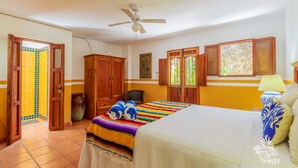 A bedroom with a bed, wooden wardrobe, ceiling fan, and a window with a view of greenery. - One Bedroom Suite, Serene, Pool, Gardens, Rooftop Terrace with Views (Isla Mujeres)