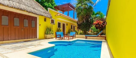 A bright yellow building with a thatched roof, a swimming pool, and outdoor seating.