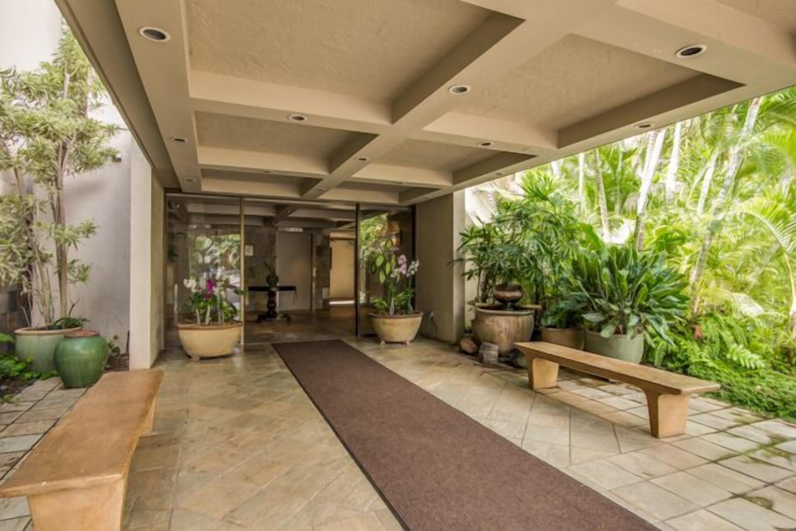A corridor with a bench, potted plants, and a view of greenery outside.