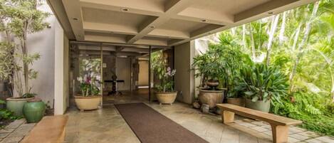 A corridor with a bench, potted plants, and a view of greenery outside.