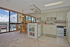 A modern kitchen with white cabinets, a dining area with a view, and a balcony.